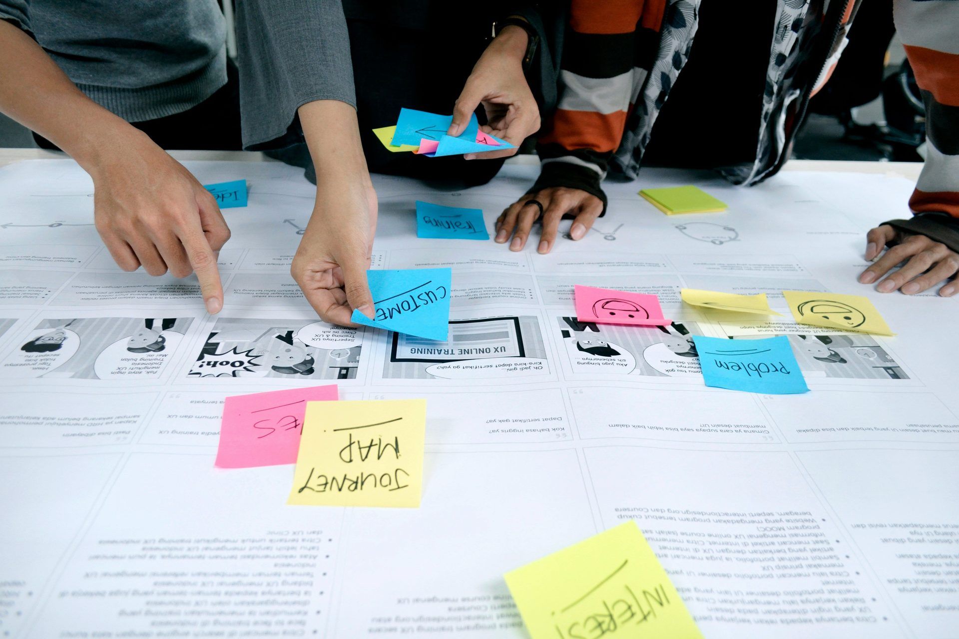 Hands placing sticky notes on a canvas during a design thinking workshop