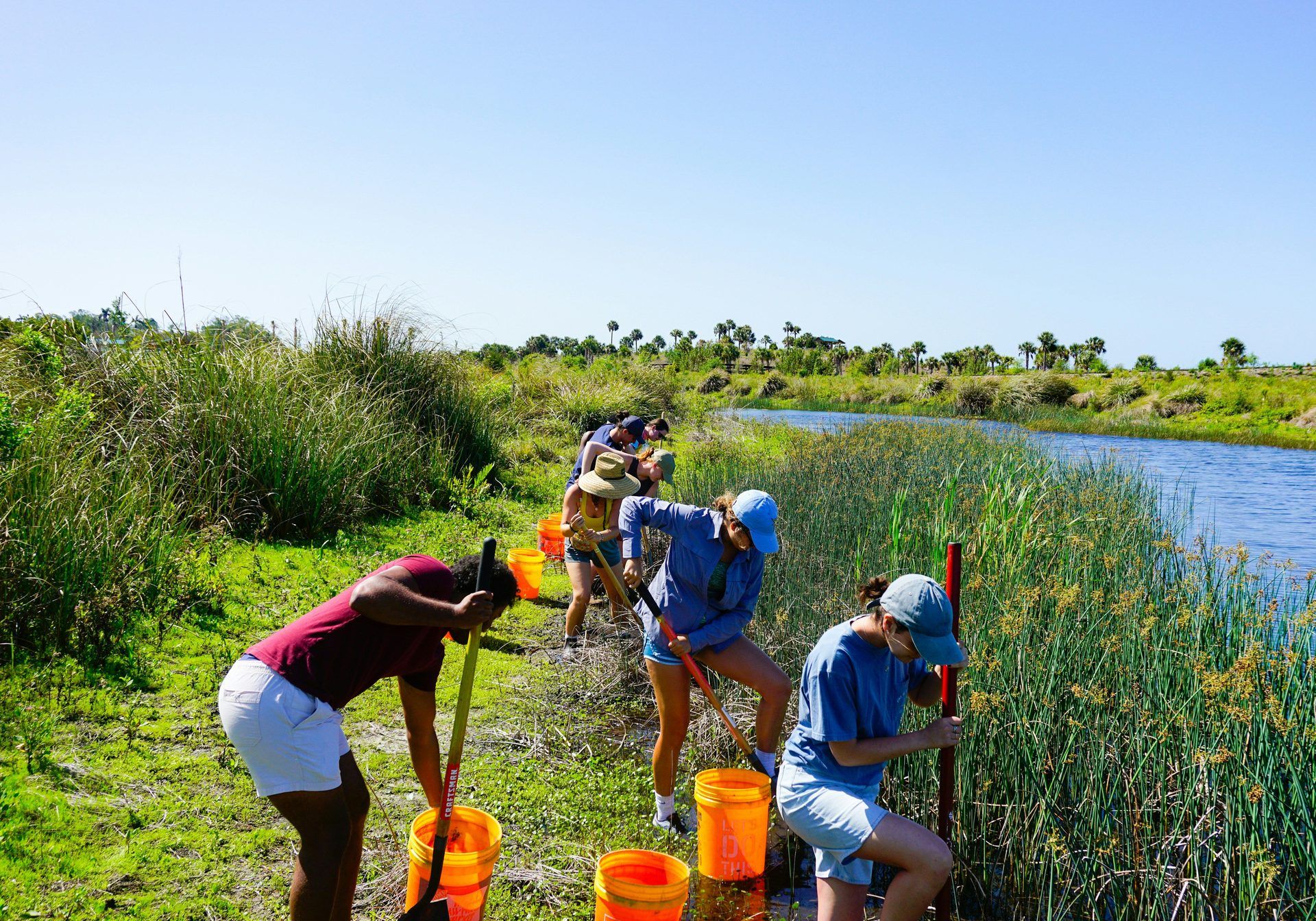Team volunteering outdoors, digging by a river bank