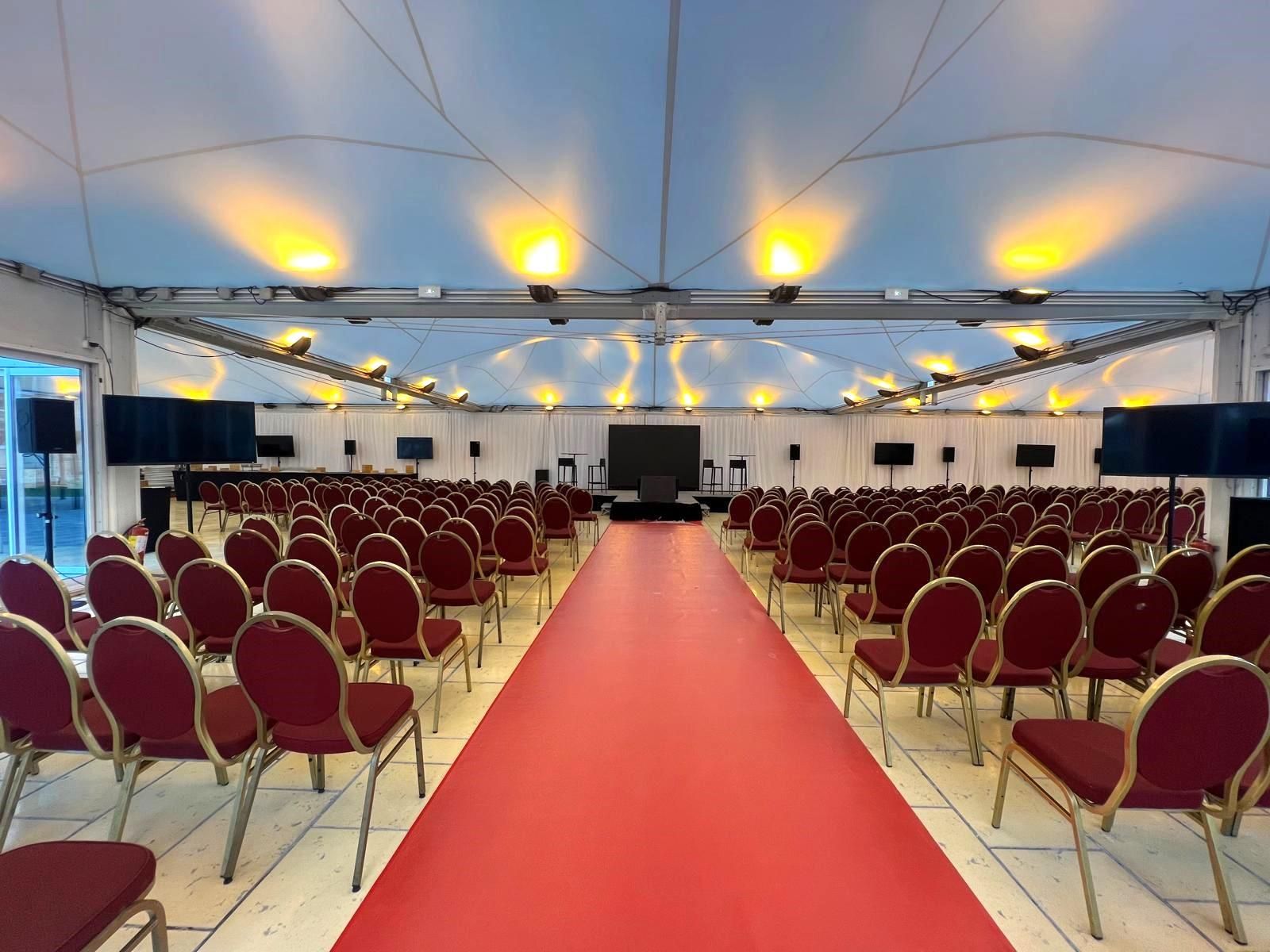 A large corporate event venue in a marquee with theater-style seating, a stage, and multiple screens.
