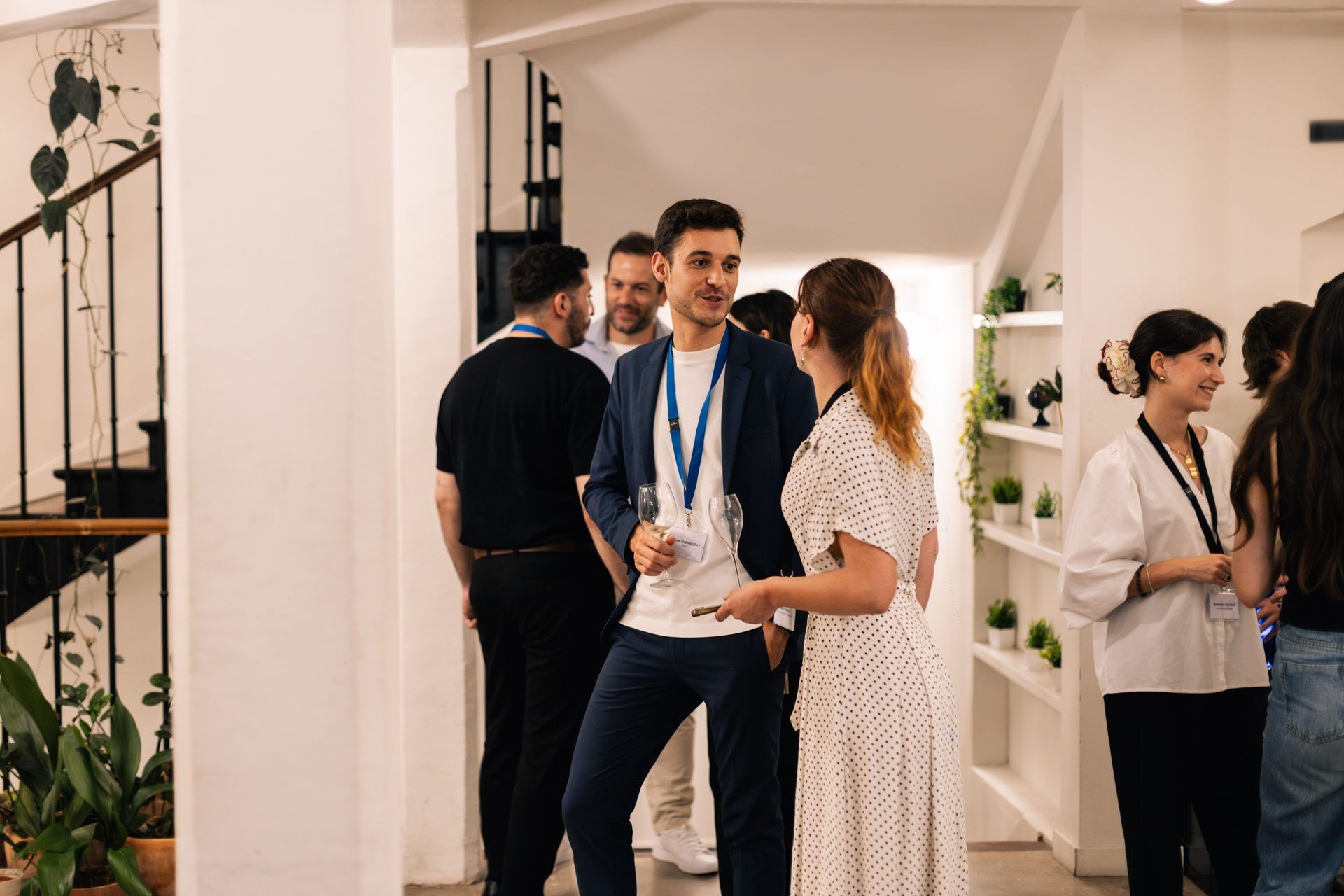 Professionals network at a corporate event, holding drinks in a modern, bright indoor event space.
