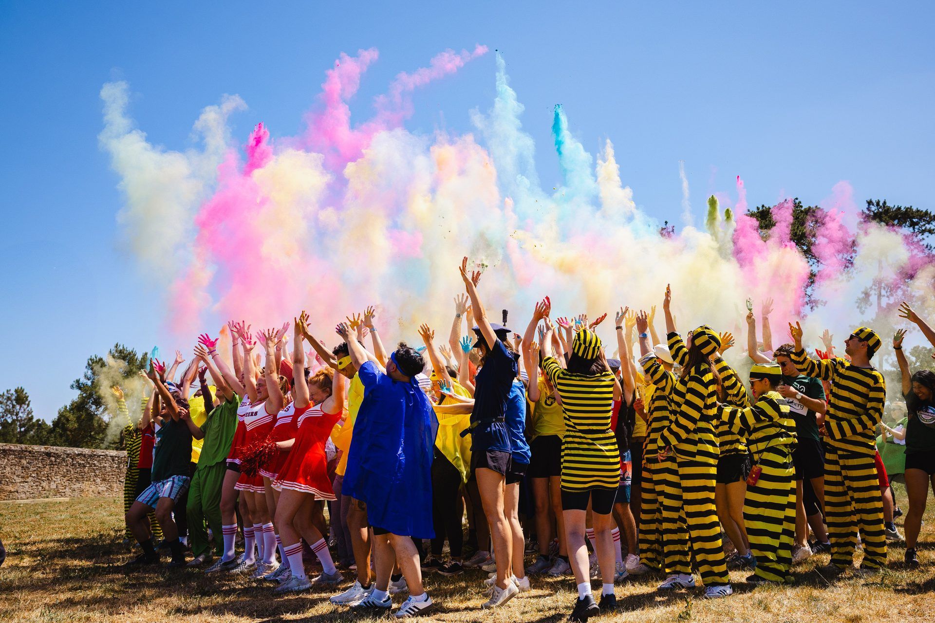 Energetic employees in costumes celebrate an outdoor team building activity with vibrant colorful powder.