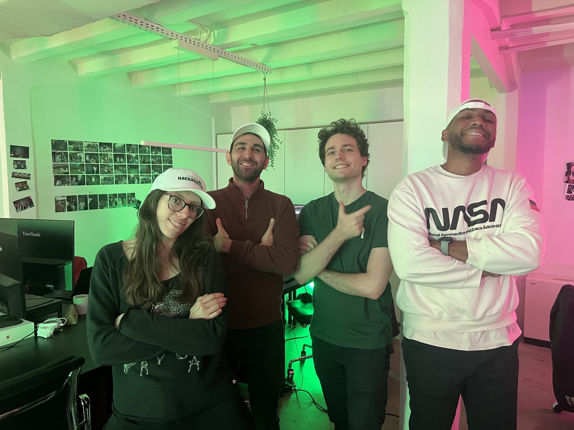 A hackathon team posing in matching caps under the green and pink neon lights