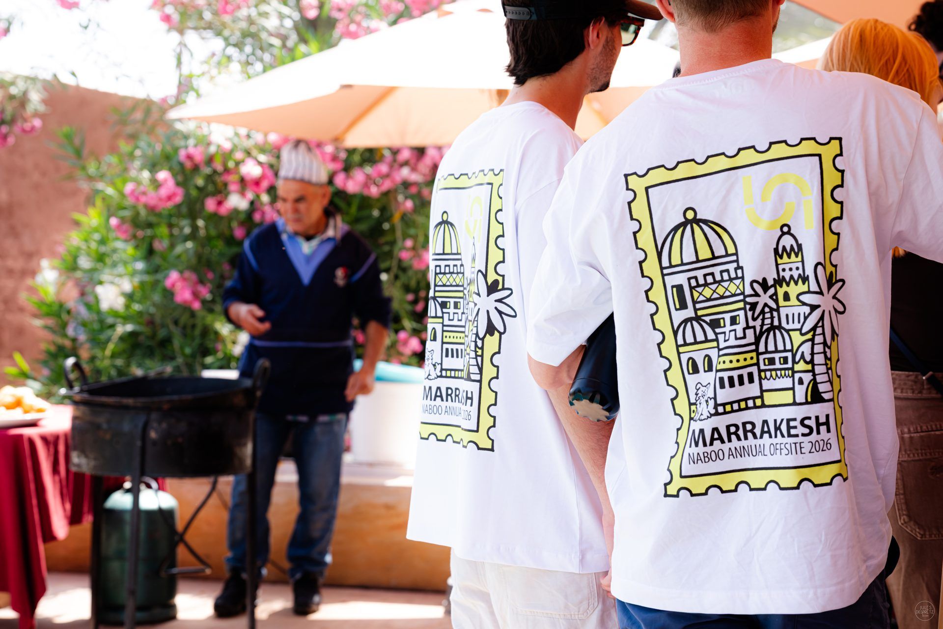 Two colleagues in the Marrakesh offsite T-shirt at the lunch grill, the stamp illustration on the back