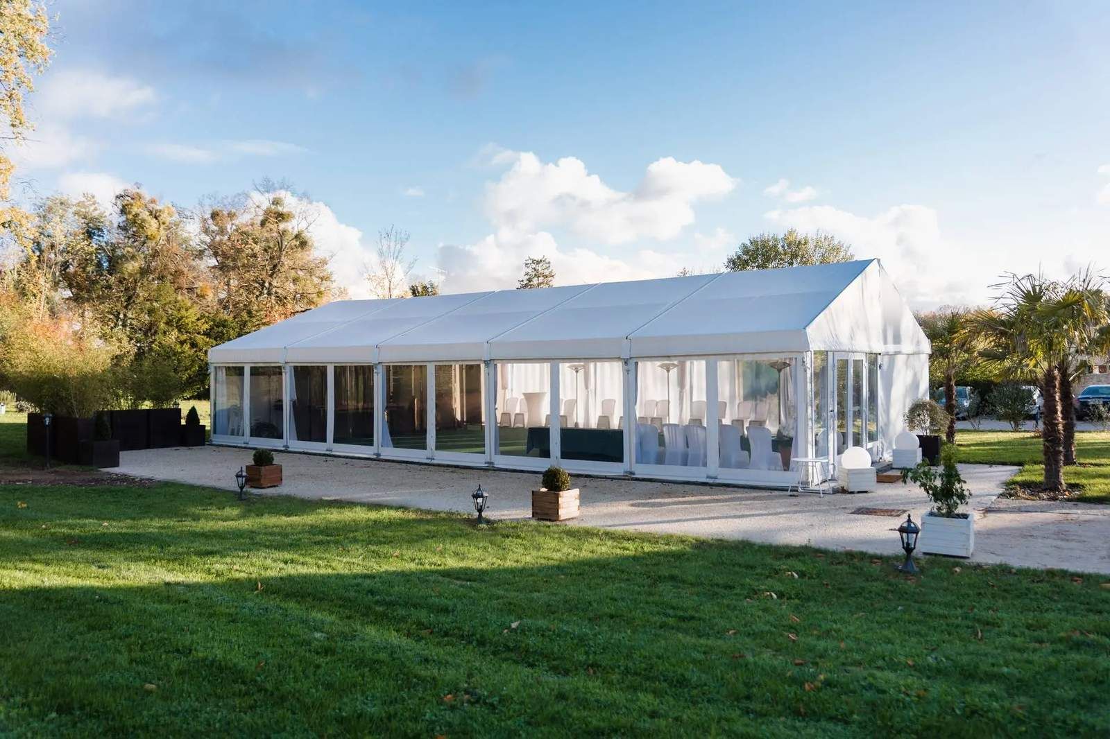 Spacious outdoor event space featuring a white marquee tent with clear walls and seating for a corporate