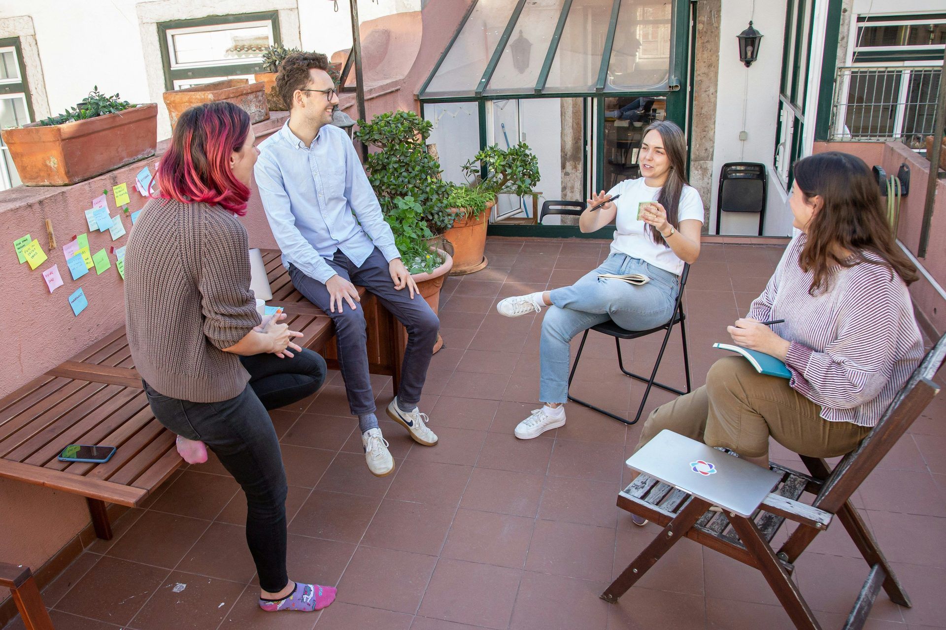 Vier Kolleg:innen bei einem lockeren Team-Offsite-Meeting auf einer Außenterrasse mit Haftnotizen an der Wand.