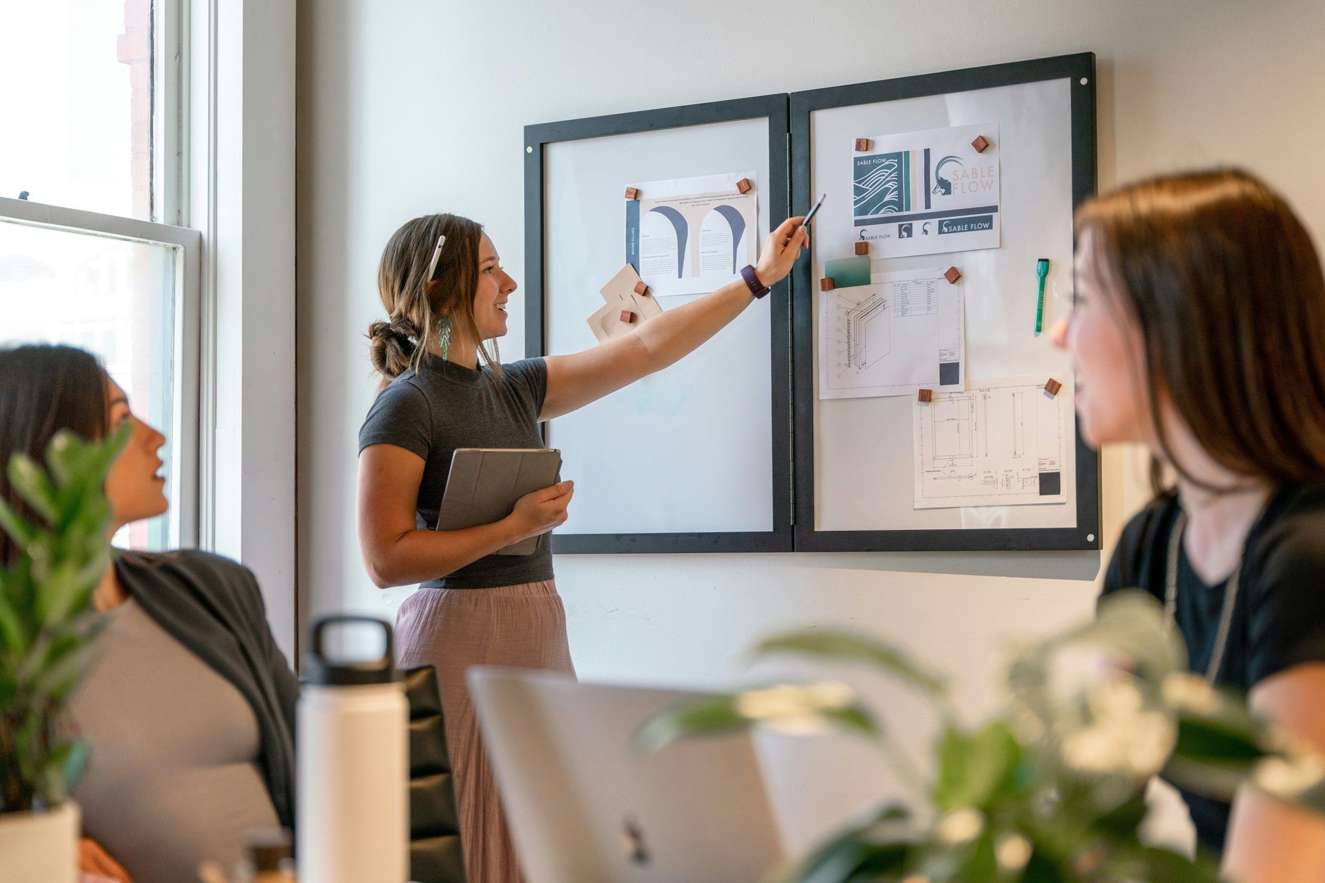 Een vrouw leidt een workshop en wijst naar een moodboard met branding- en designconcepten in een moderne vergaderruimte.
